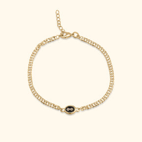 Goudkleurige armband met ovale bruine steen in het midden op een lichte achtergrond.